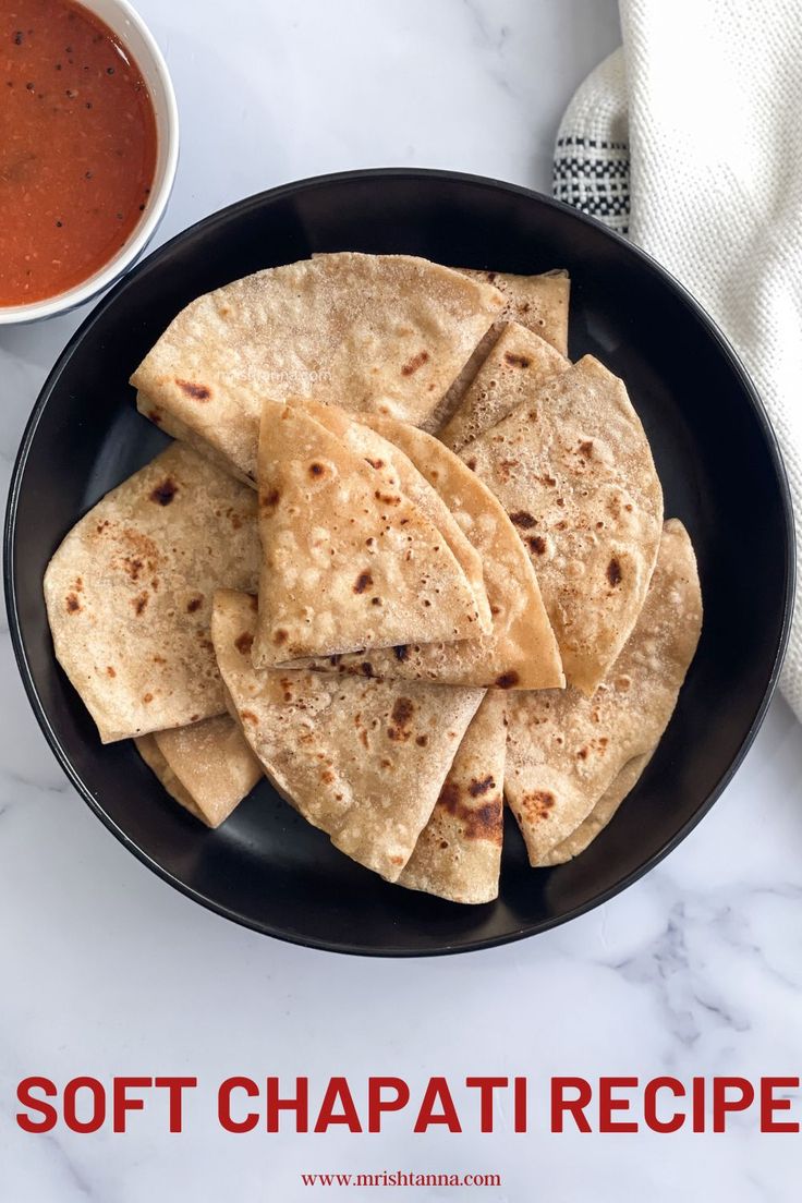 a black plate topped with tortillas next to a bowl of salsa and a napkin