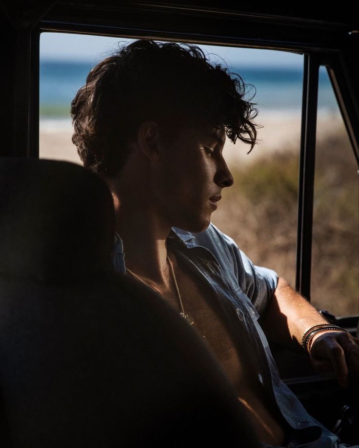 a man sitting in the back seat of a car looking out at the ocean and sand