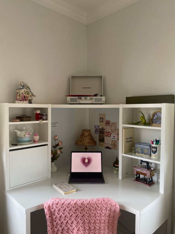 a laptop computer sitting on top of a white desk next to a shelf filled with books