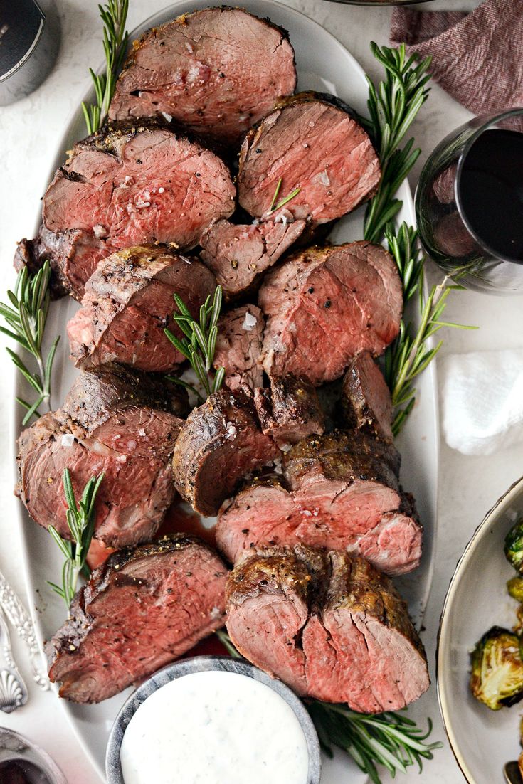 steak and vegetables on a platter next to wine glasses, sauces and utensils