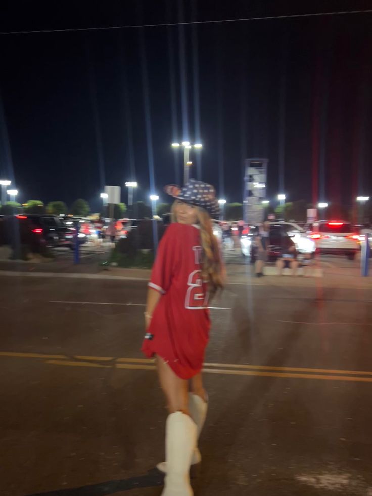 a woman is walking down the street at night wearing white boots and a red dress