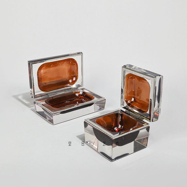 two square shaped glass dishes sitting next to each other on a white surface with one being filled with liquid