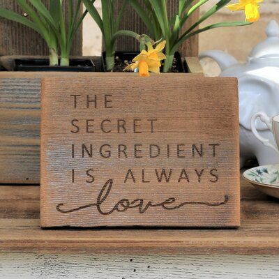 a wooden sign that says the secret ingredient is always love with daffodils