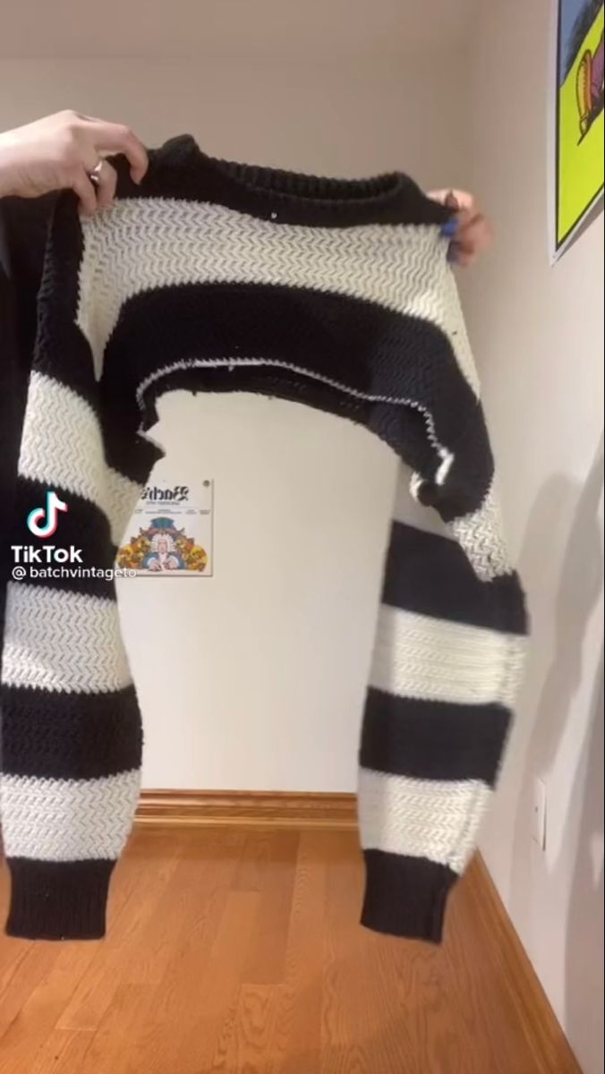 someone is holding up a black and white sweater