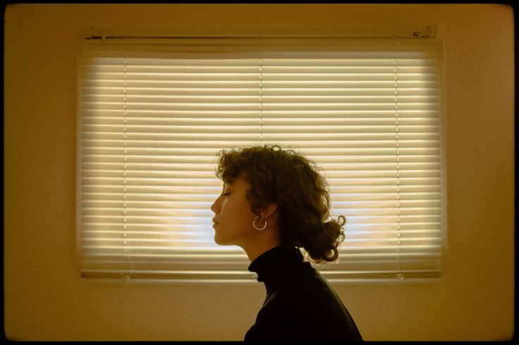 a woman standing in front of a window with blinds