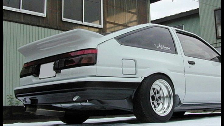 the back end of a white car parked in front of a building with snow on the ground