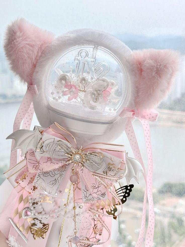 a pink and white teddy bear with bows on it's head sitting next to a window