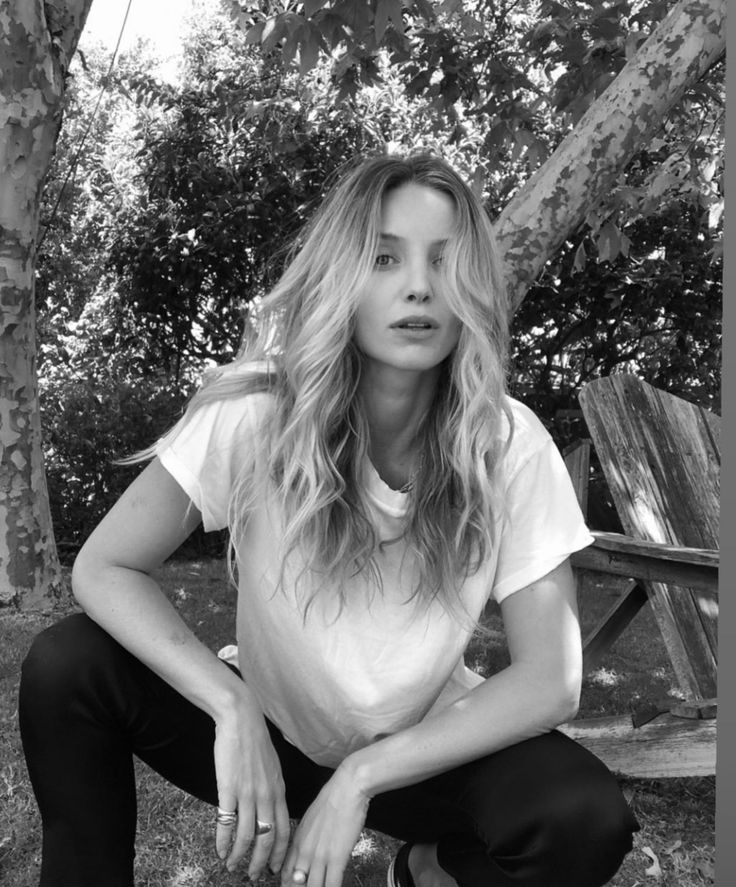 a black and white photo of a woman sitting on a park bench with her hands in her pockets