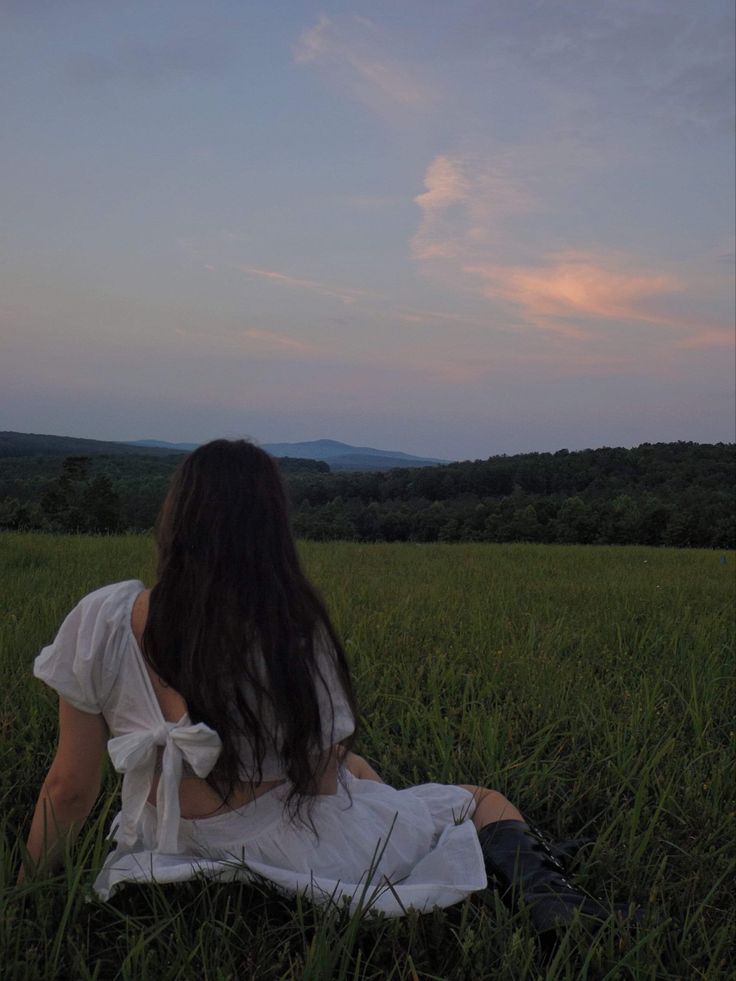 a woman sitting in the middle of a field with her back turned to the camera