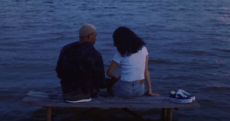 two people sitting on a bench looking at the water