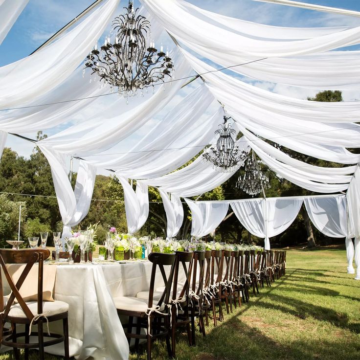 an outdoor wedding setup with white drapes and chandelier