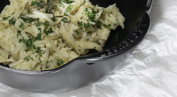 pasta with parsley in a black bowl on a white tableclothed surface, ready to be eaten