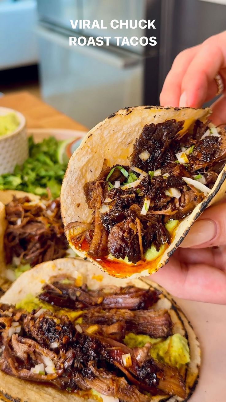 a person is holding up a taco with meat and vegetables on it, while another hand holds the food in front of them