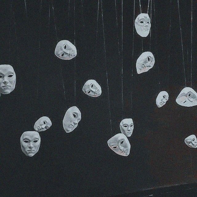 several masks hanging from strings in front of a black wall with white faces on them