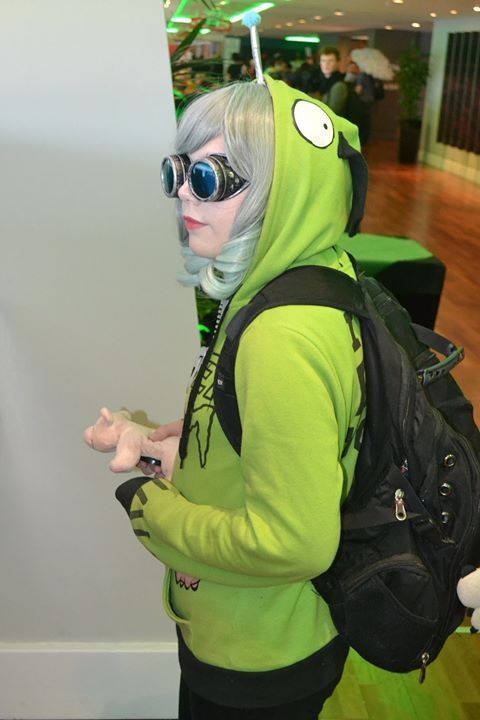 a woman with grey hair wearing sunglasses and a green hoodie standing in front of a white wall