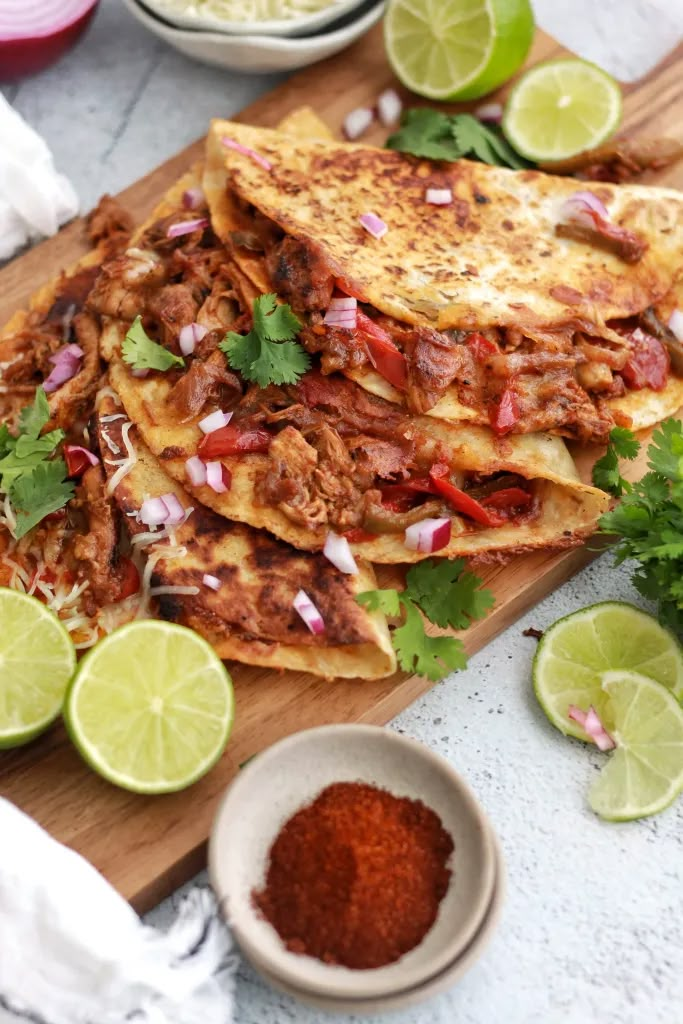 pulled chicken tacos on a cutting board with limes and cilantro in the background