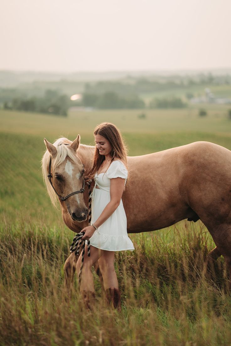 a woman in white dress standing next to a brown horse