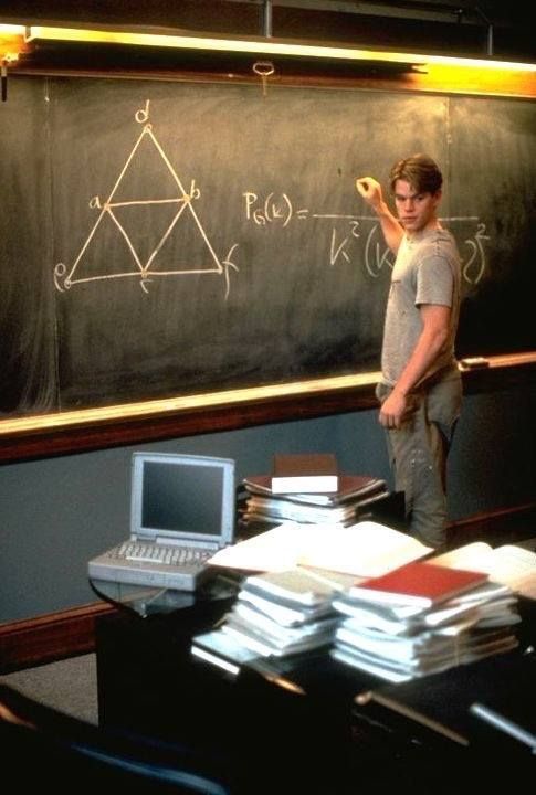 a man standing in front of a blackboard with papers on it and a laptop