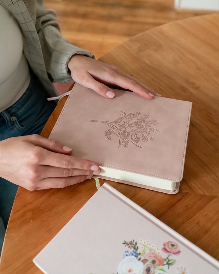 a woman sitting at a table with a book and pen in her hand next to it