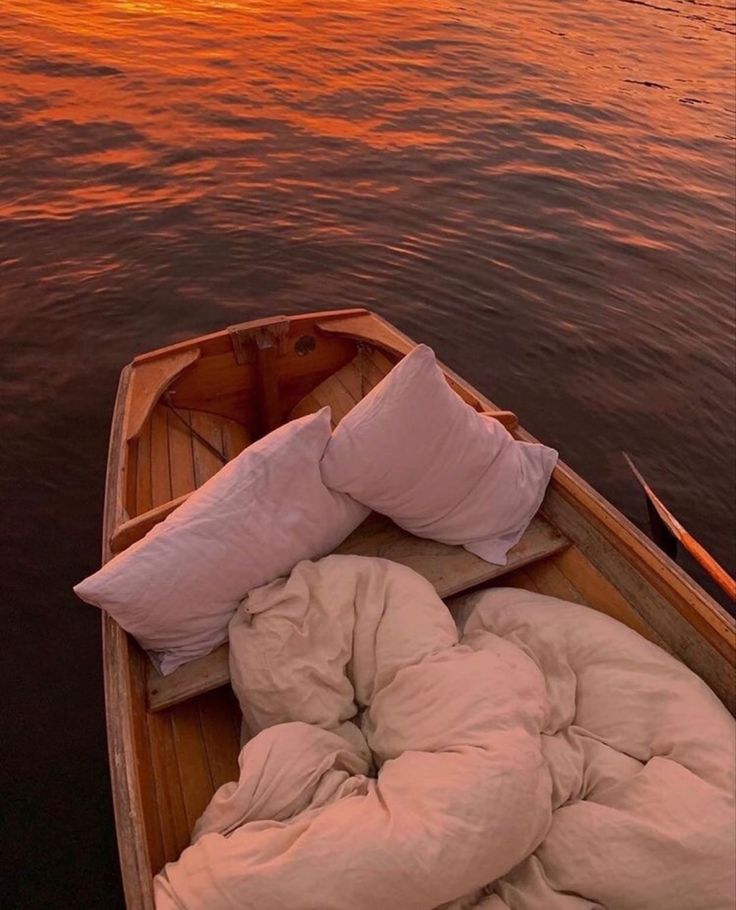 a small boat with pillows and blankets on it in the water at sunset or dawn