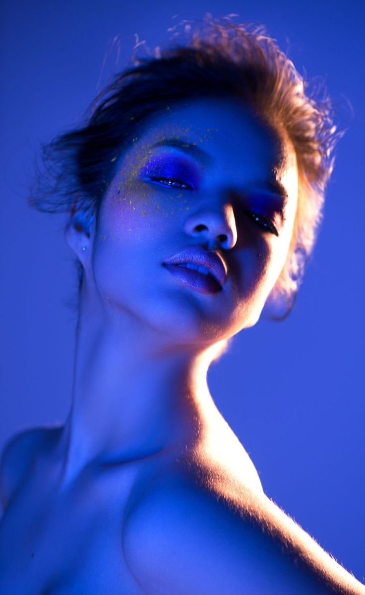 a naked woman with blue light on her face and chest, posing for the camera