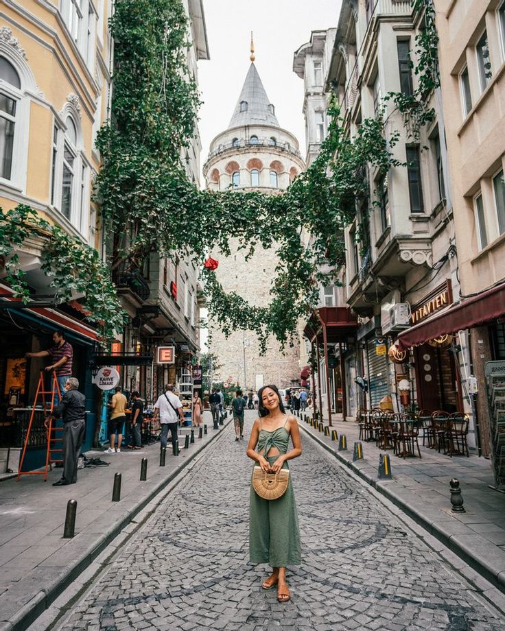 a woman is standing in the middle of an alleyway with buildings and trees on both sides