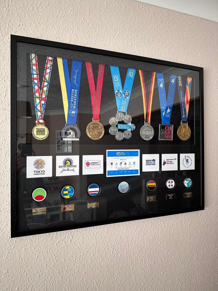 a group of medals on display in a black frame hanging on the wall next to a white wall