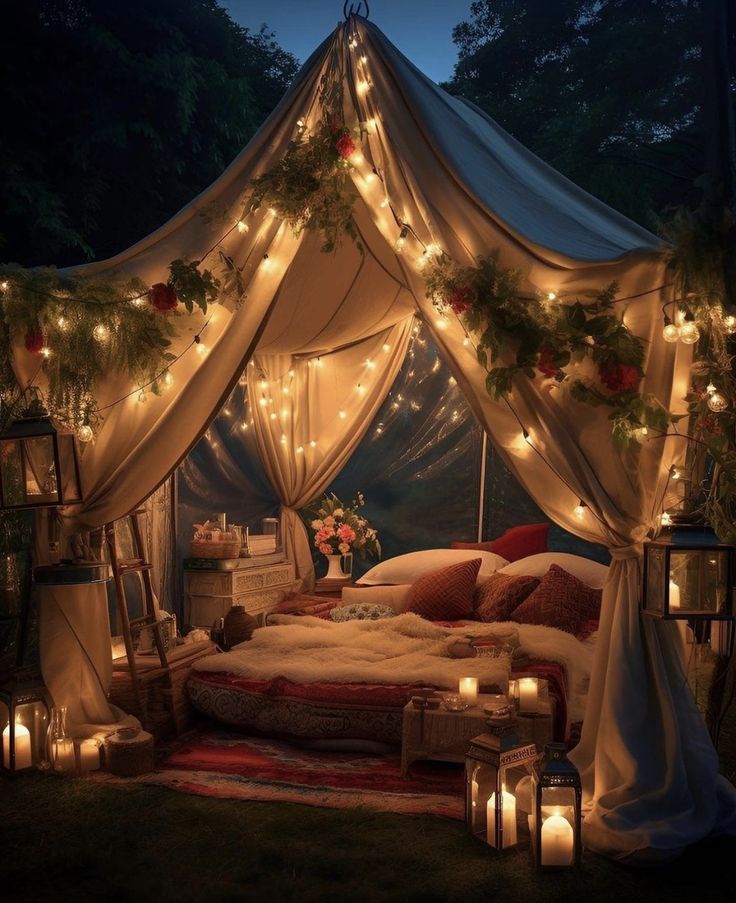 a bed covered in lights and surrounded by greenery with candles on the floor next to it