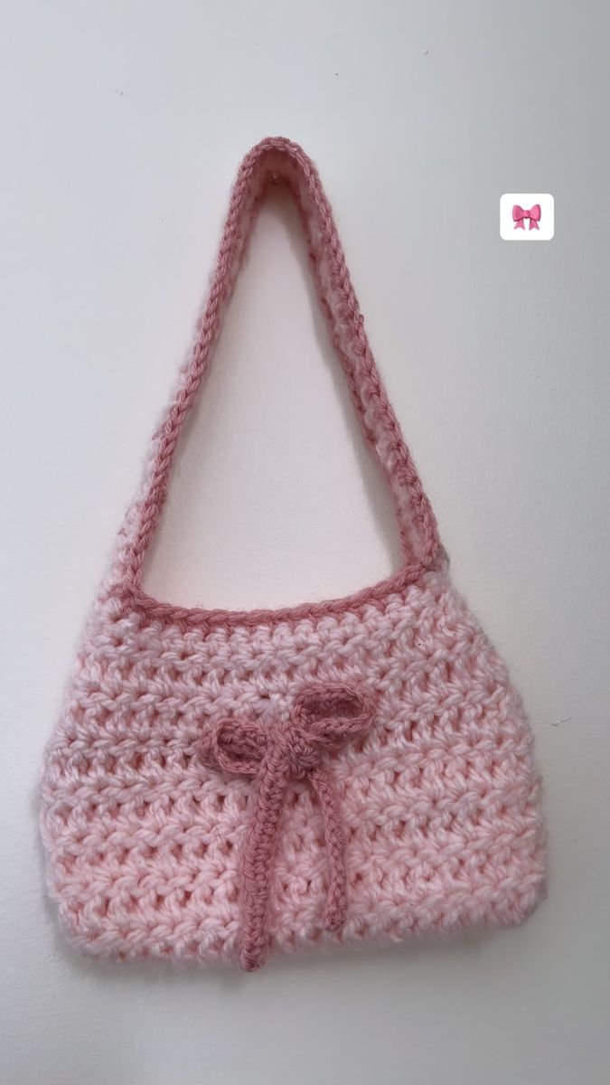 a pink crocheted purse hanging on the wall with a bow at the top