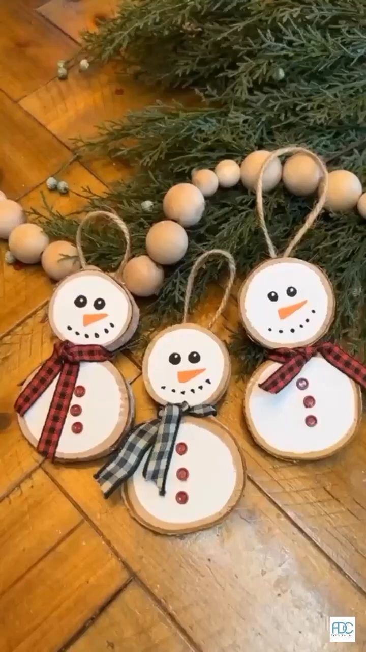 four snowman ornaments hanging from a christmas tree on a wooden floor with baubles around them