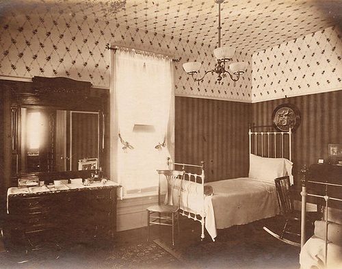 an old black and white photo of a bedroom with a bed, dresser, mirror and chair