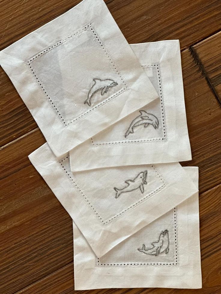 four napkins with embroidered dolphins on them sitting on a wooden floor next to each other