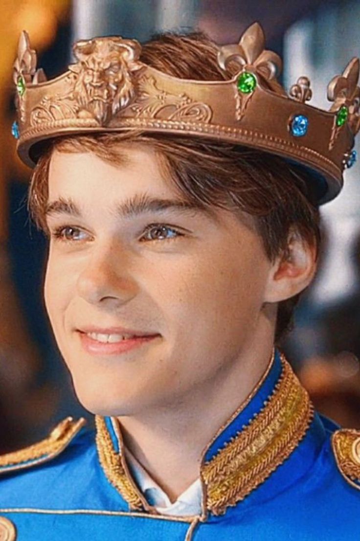 the young man is wearing a gold crown and blue suit with green jewels on his head