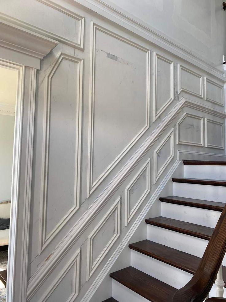 a white staircase with wood handrails and paneling on the wall next to it