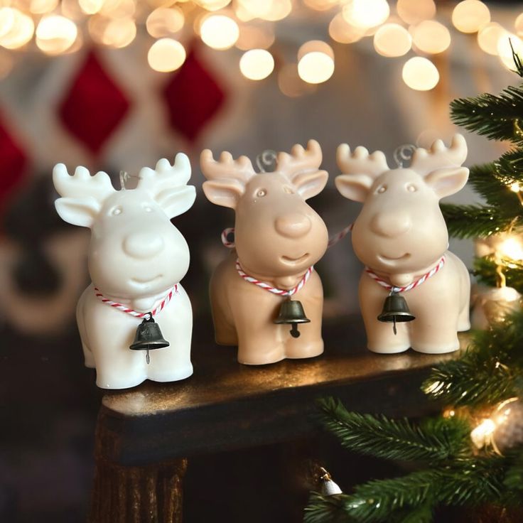 three small ceramic reindeer figurines on a mantle with christmas lights in the background