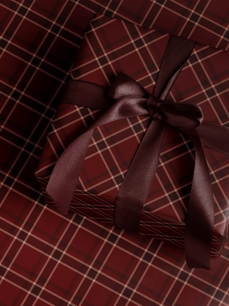 a present wrapped in brown ribbon on a red plaid table cloth with a bow at the top