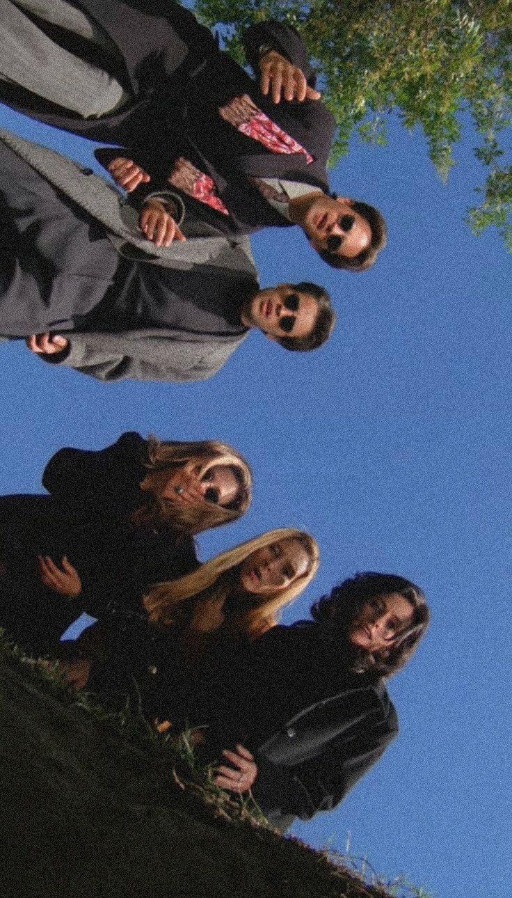 four people are standing in front of a tree and one person is taking a selfie