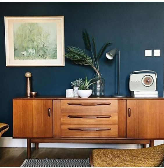 a living room with blue walls and wooden furniture, including a sideboard that has plants on it