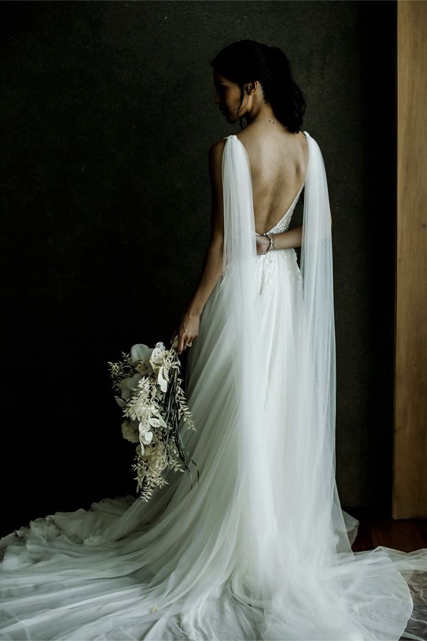 a woman in a white wedding dress holding a bouquet and looking down at the floor