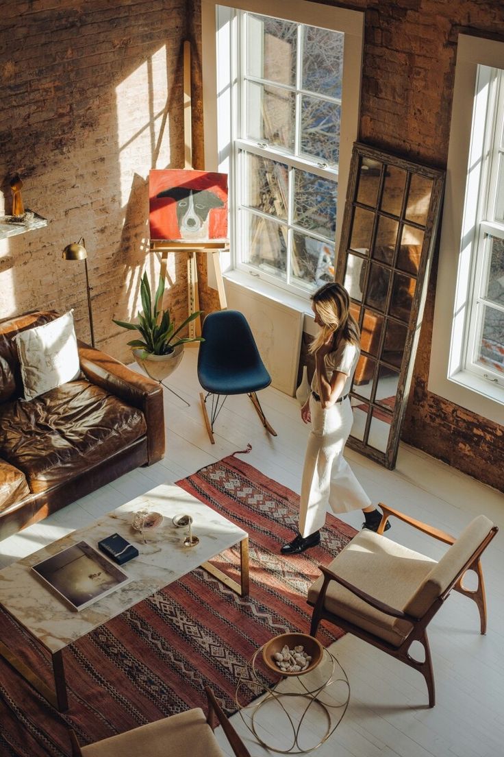 a woman standing in the middle of a living room with chairs and rugs on the floor