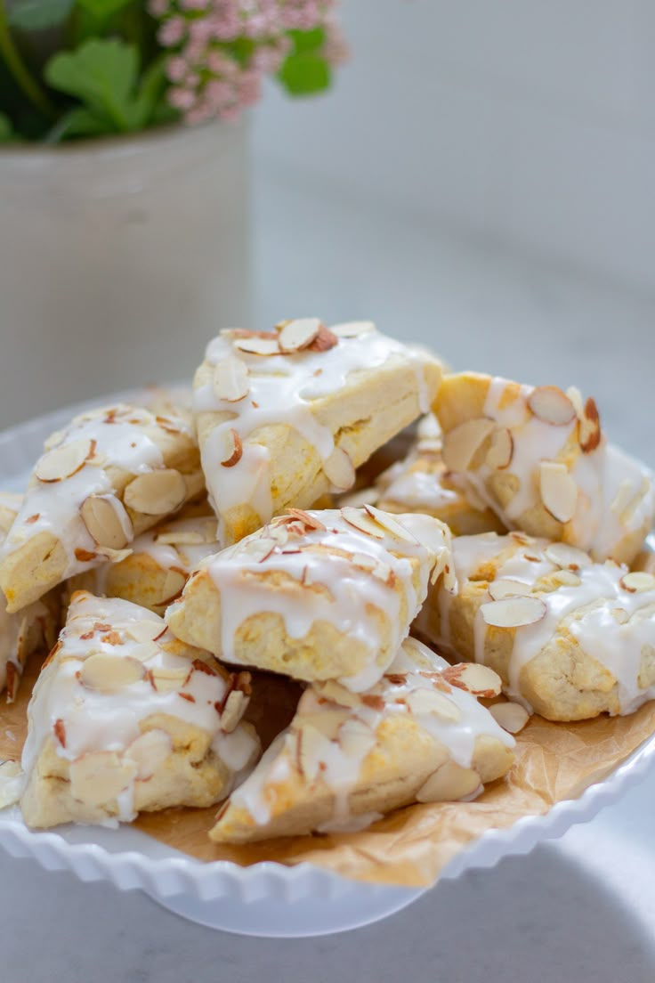 a white plate topped with sliced bananas covered in icing and almonds next to a potted plant