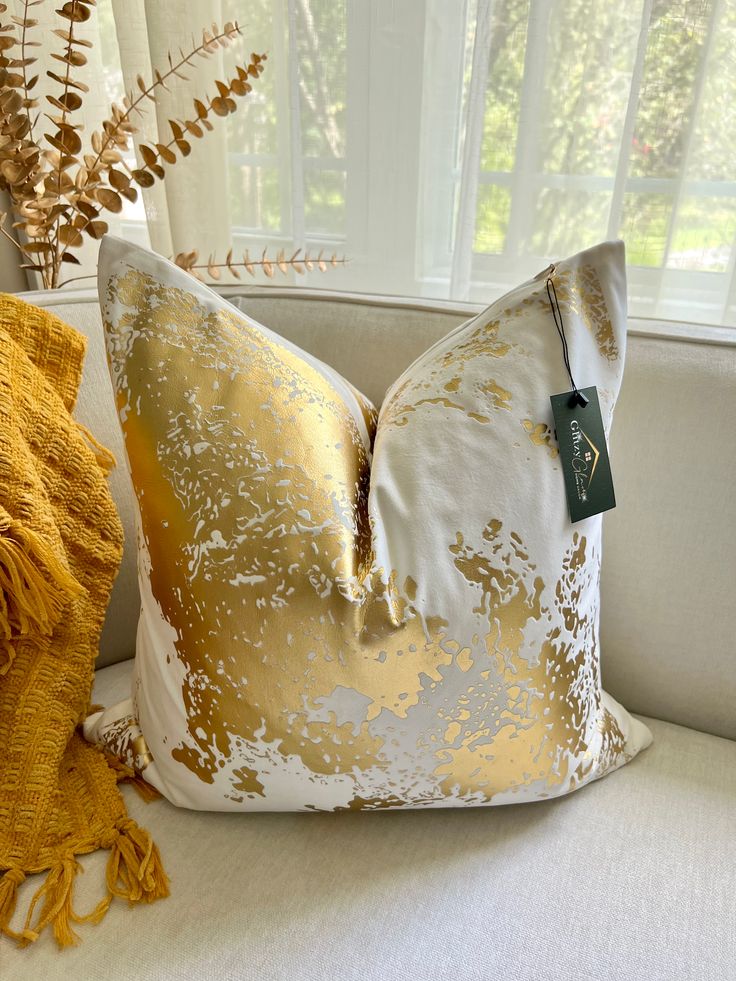 a white and gold pillow sitting on top of a couch next to a window sill