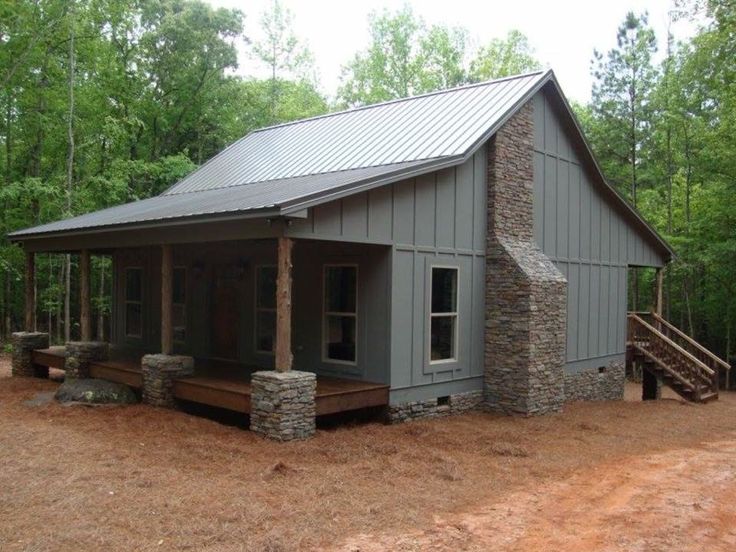 a small gray cabin in the woods with stairs leading up to it's front door