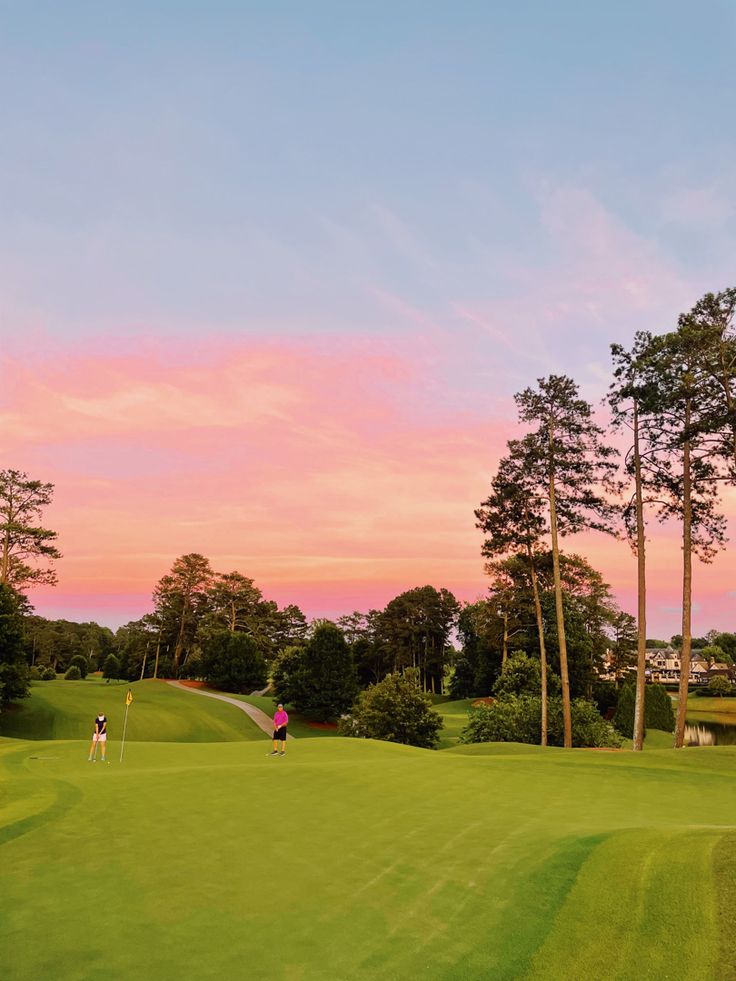 two people are playing golf on a green course at sunset or dawn with trees in the background