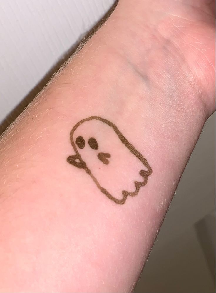 a small tattoo on the wrist of a person with a ghost face drawn on it