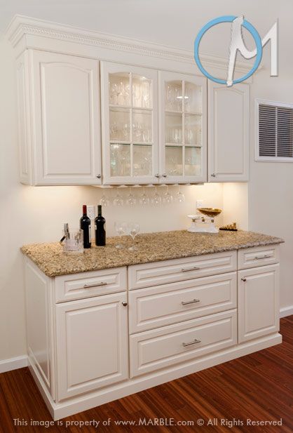 a kitchen with white cabinets and marble counter tops, wine glasses on the cabinet doors