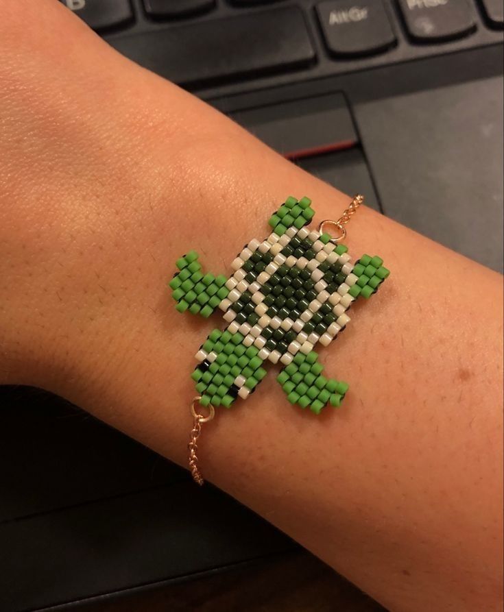 a person's arm with a green and white beaded turtle bracelet on it