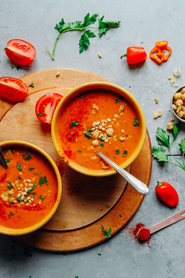 two bowls of tomato soup on a cutting board with tomatoes, chickpeas and parsley