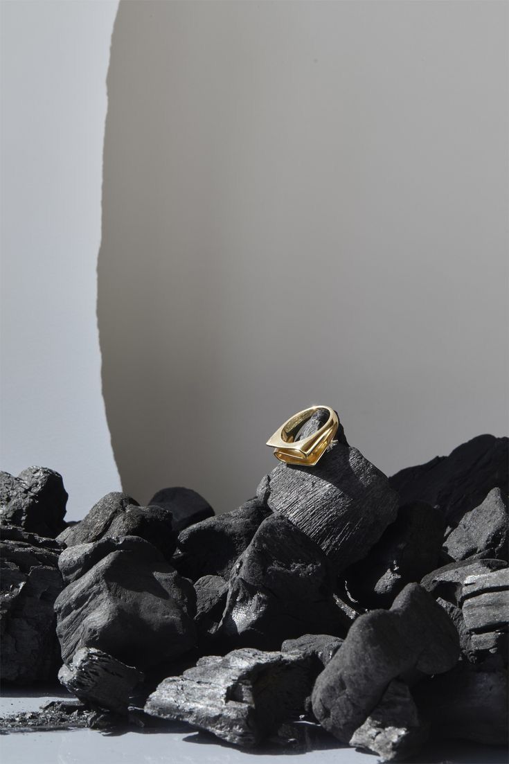 a gold ring sitting on top of some rocks next to a white wall and black rock