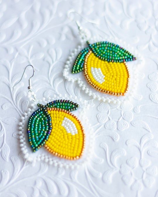 two beaded fruit earrings sitting on top of a white table